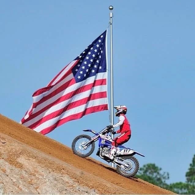 A rider climbing a dirt hill beneath an American flag