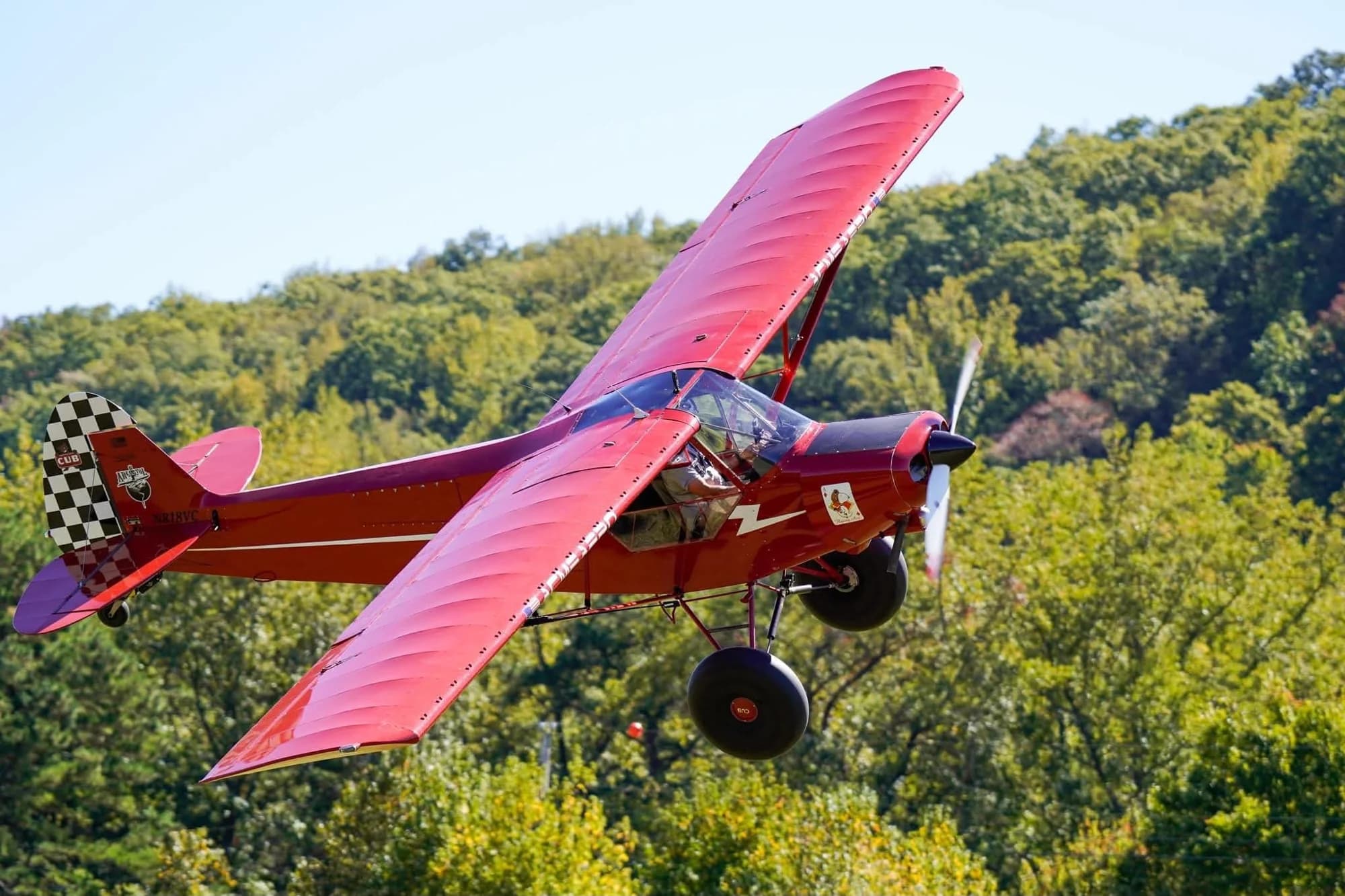 A red bush plane flying low over green trees