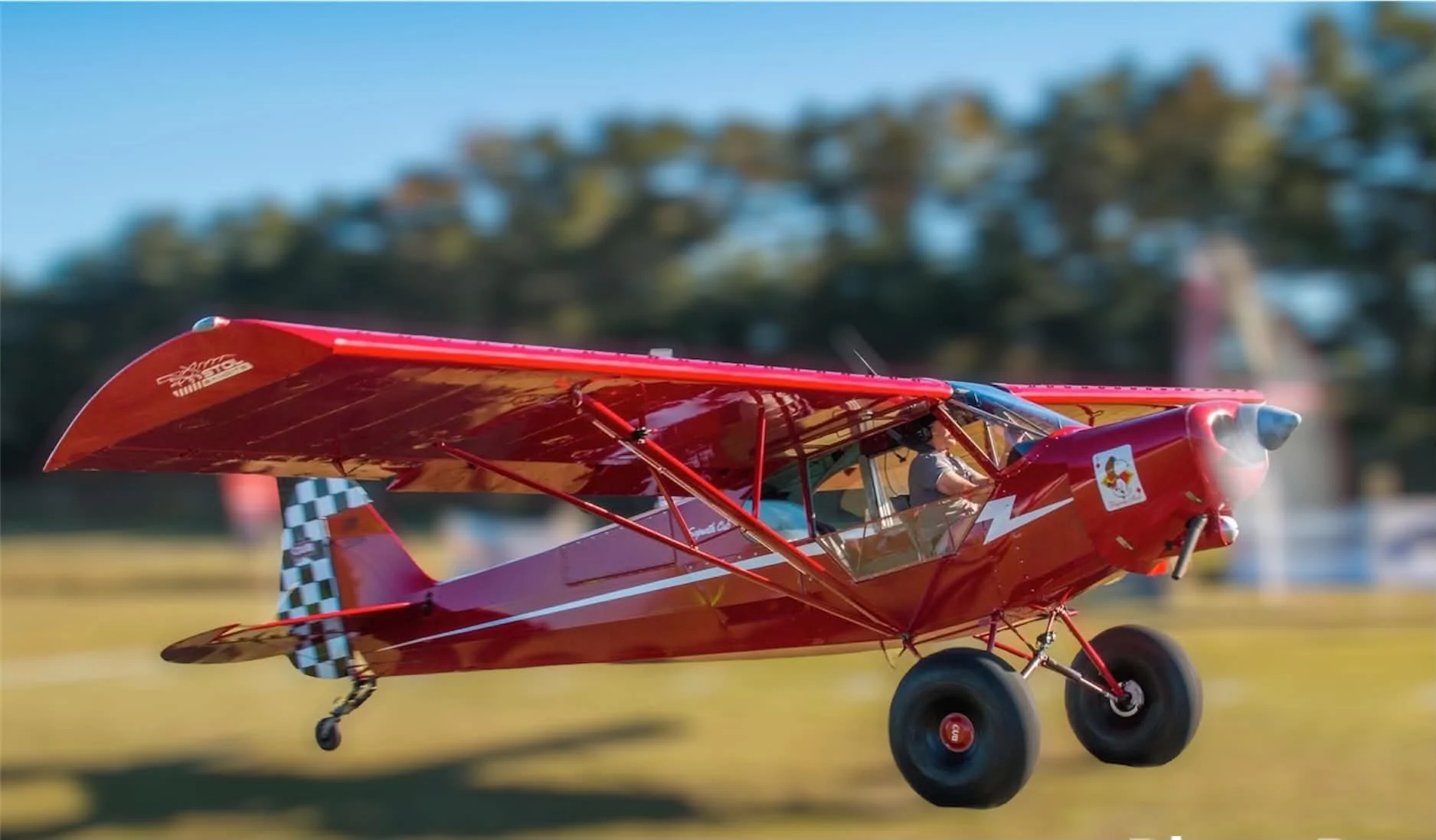 A red bush plane taking off from a grass field