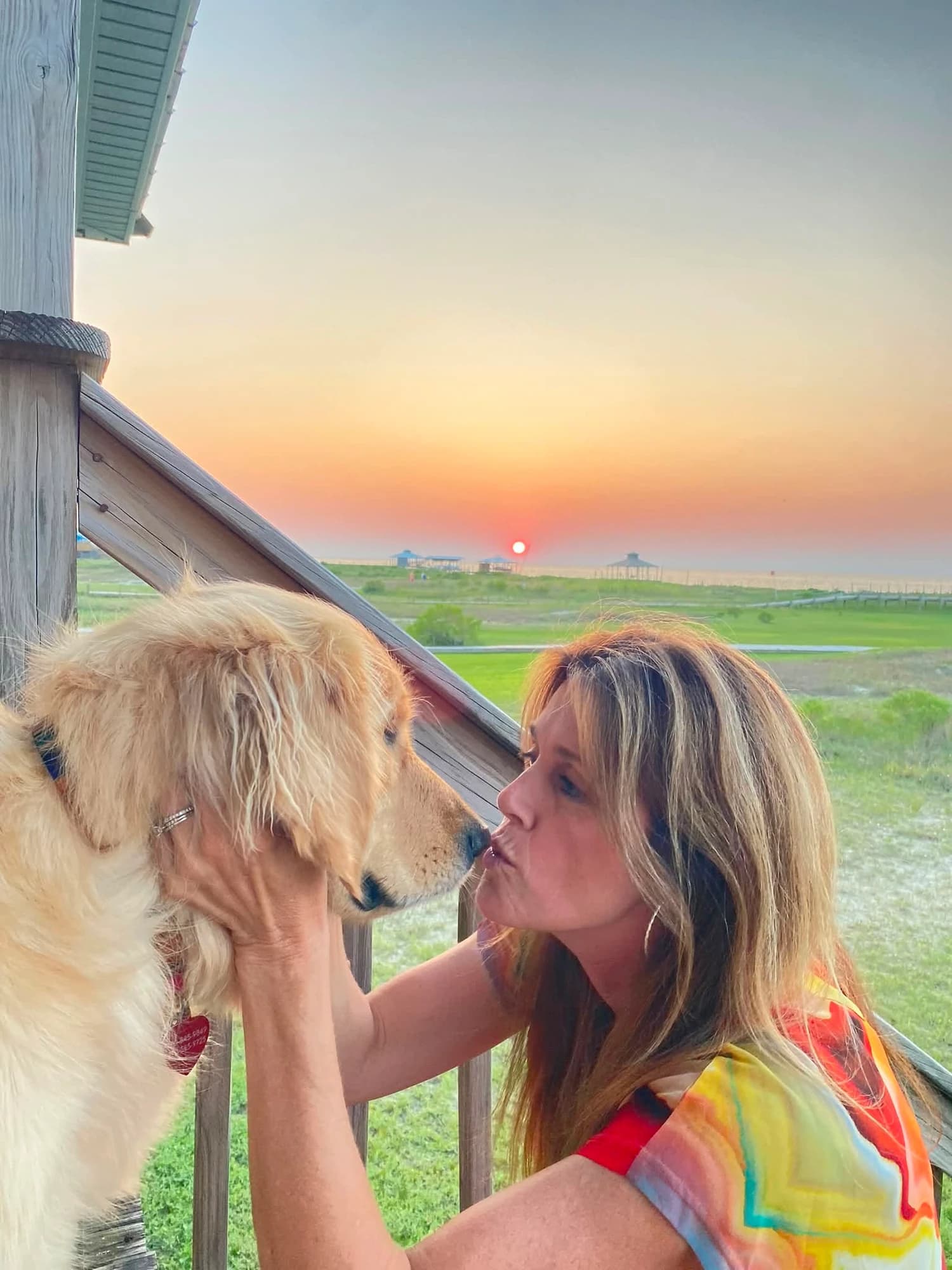 A woman kissing a golden retriever at sunset