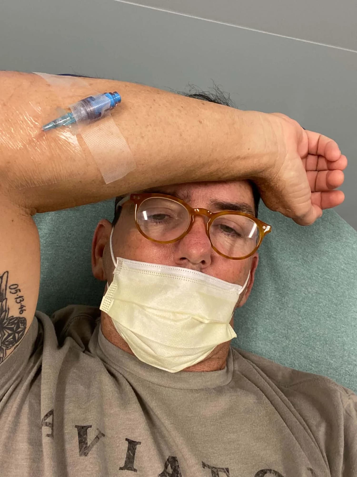 Frank resting in a hospital bed with a mask on, arm across his forehead