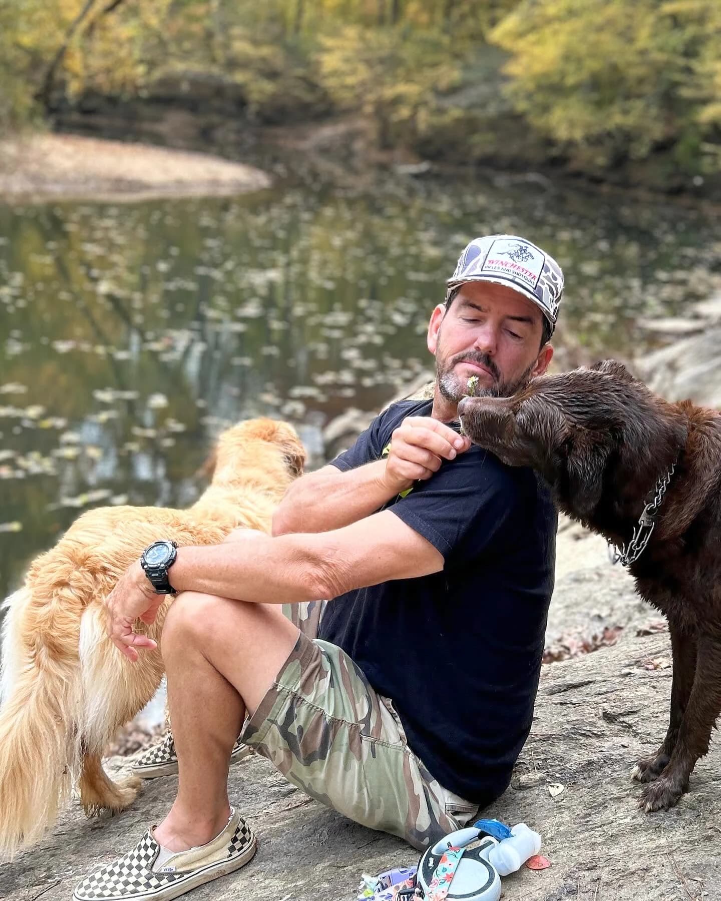 Frank sitting by a creek with his two dogs